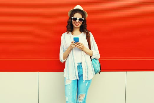 happy smiling young woman with smartphone in summer hat with backpack on red background