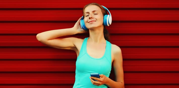Portrait of fitness smiling young woman in headphones listening to music with smartphone