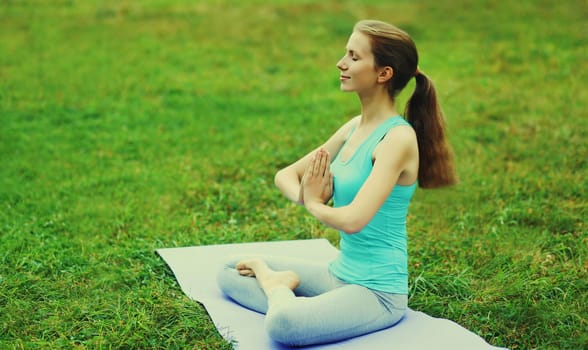 Young woman doing yoga exercises on a mat on the grass in summer park