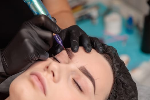 Beautician making permanent eyebrow makeup correction on young woman in beauty salon