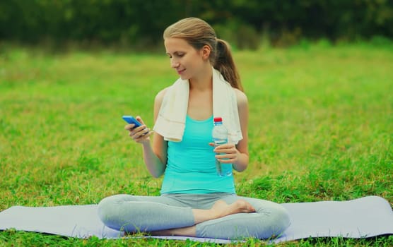 Fitness woman with smartphone on a mat on the grass in summer park