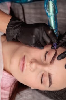 Cosmetologist making permanent eyebrow makeup by tattooing machine