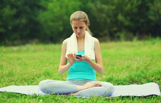 Fitness woman with smartphone on a mat on the grass in summer park