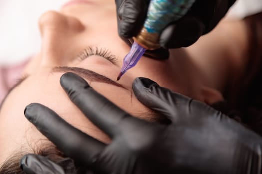 Beautician is making permanent eyebrow makeup for a brunette woman in a beauty salon