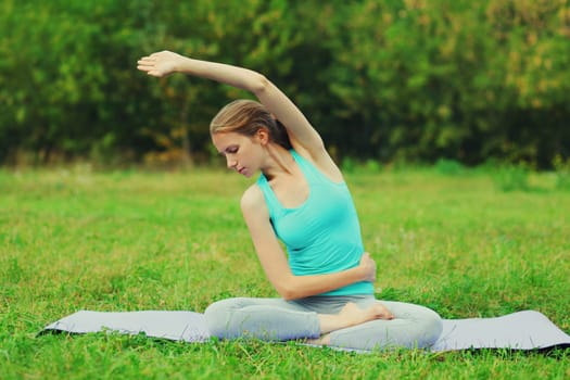Fitness woman doing yoga exercises back stretching on a mat on the grass in summer park