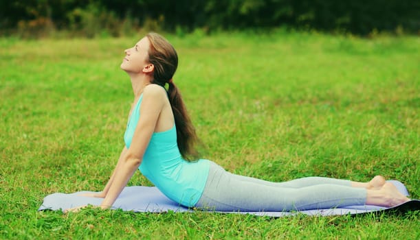 Fitness woman doing yoga exercises back stretching on a mat on the grass in summer park