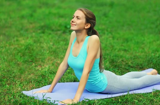 Fitness woman doing yoga exercises back stretching on a mat on the grass in summer park