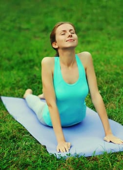 Fitness woman doing yoga exercises back stretching on a mat on the grass in summer park