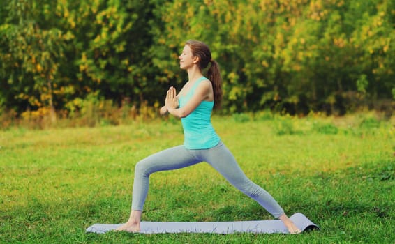 Fitness woman doing yoga exercises on a mat on the grass in summer park