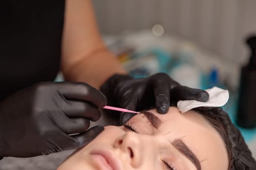 Beautician is applying permanent eyebrow makeup on a client's face in a beauty salon