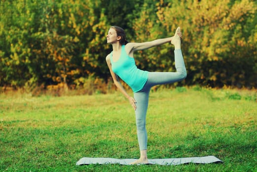 Fitness woman doing yoga exercises on a mat on the grass in summer park