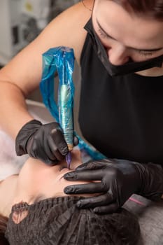 Beautician performing permanent eyebrow makeup on a client in a beauty salon