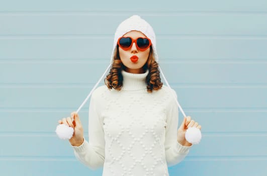 Happy woman blowing kiss wearing a heart shape sunglasses, knitted hat, sweater over blue background