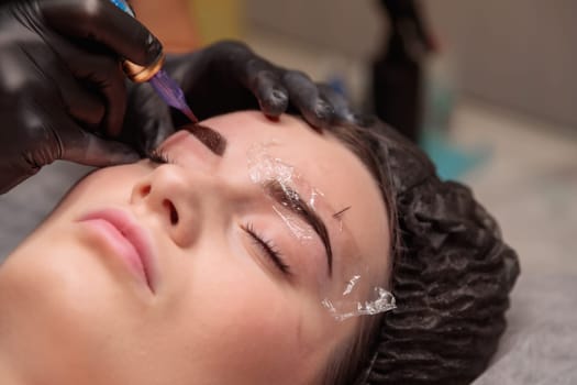 Beautician is making permanent eyebrow makeup for a client in a beauty salon