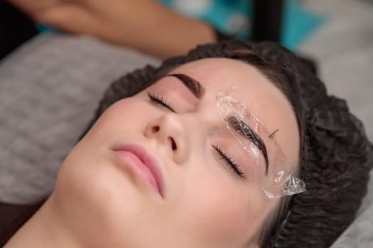 Beautician is applying permanent makeup on eyebrows of her client in a beauty salon