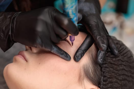 Beautician performing permanent eyebrow makeup tattooing procedure on young woman in beauty salon