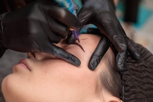Beautician performing microblading procedure on eyebrows of client in beauty salon