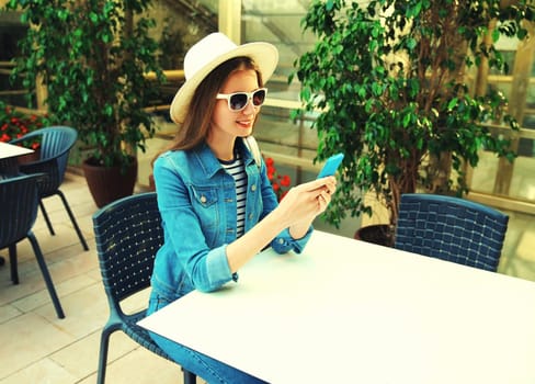 Portrait of smiling young woman sitting at table in cafe with phone