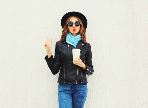 Fashion cool girl with coffee cup blowing a kiss wearing black rock jacket over white background