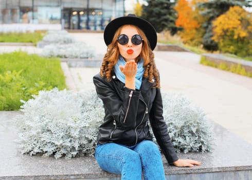 Fashion portrait young woman blowing a kiss wearing black hat in city park
