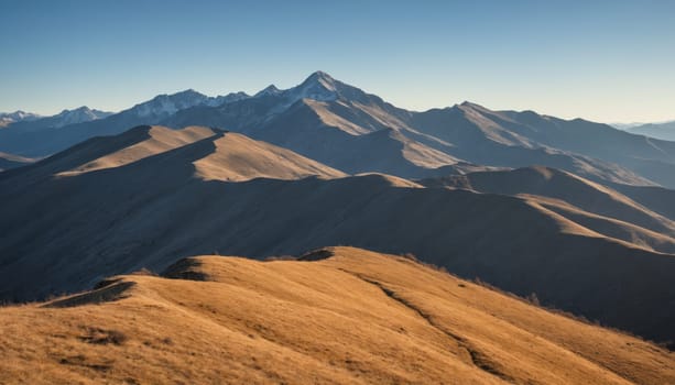 Golden grasses blanket the rolling hills as majestic mountains rise in the distance, illuminated by the soft glow of morning sunlight against a pristine blue backdrop.