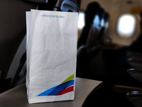 An airsickness bag with a colorful airline logo rests on an airplane seatback tray.