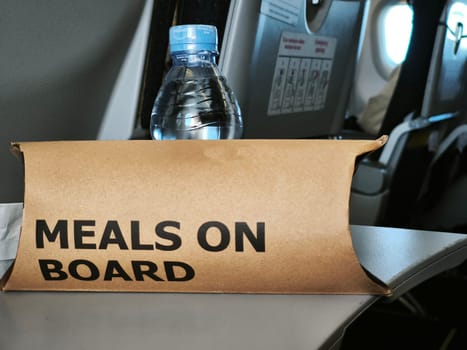 Meal box with Meals on Board text on an airplane seat, with a bottle of water on top.