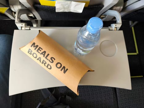 Meal box with Meals on Board text on an airplane seat, with a bottle of water on top.