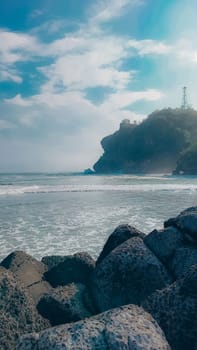 A rocky shoreline with a large rock formation in the background. The water is calm and the sky is blue