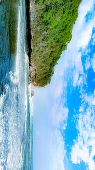 A rocky shoreline with a large rock formation in the background. The water is calm and the sky is blue