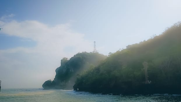 A rocky shoreline with a large rock formation in the background. The water is calm and the sky is blue