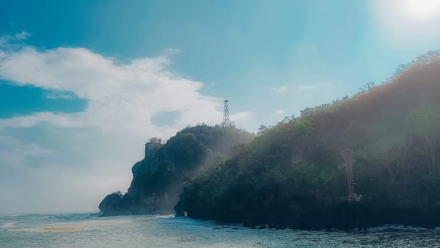 A rocky shoreline with a large rock formation in the background. The water is calm and the sky is blue