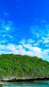 A rocky shoreline with a large rock formation in the background. The water is calm and the sky is blue