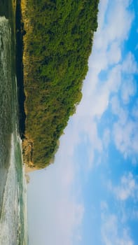 A rocky shoreline with a large rock formation in the background. The water is calm and the sky is blue