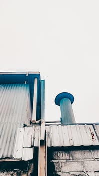 A low-angle view of an industrial building's exterior features metal pipes and a chimney against a clear sky, emphasizing architecture and industrial design.