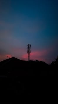 A silhouette of a communication tower stands prominently against a stunning pink and blue sky at sunset, evoking a sense of tranquility and modern technology.