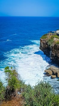 Stunning view of a rocky cliff overlooking the vast, blue ocean with waves crashing below. The harmonious blend of sea and sky offers a sense of peace and tranquility.
