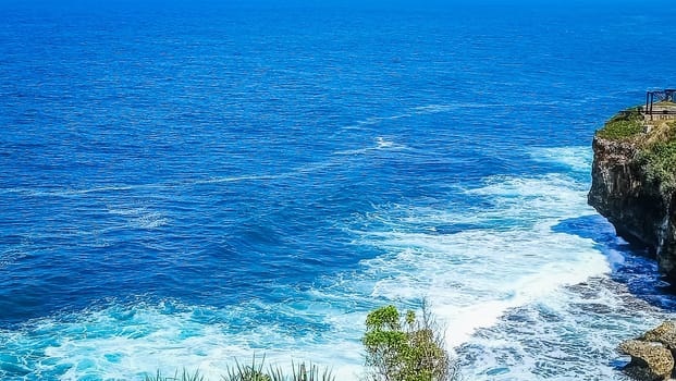 Stunning view of a rocky cliff overlooking the vast, blue ocean with waves crashing below. The harmonious blend of sea and sky offers a sense of peace and tranquility.