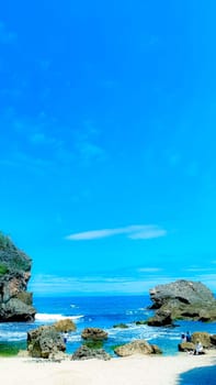 A serene beach setting with clear blue skies, rocks, and gentle sea waves. Perfect for representing relaxation, nature, and tranquility in a coastal environment.