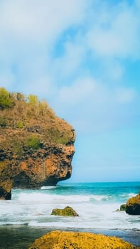 A serene beach setting with clear blue skies, rocks, and gentle sea waves. Perfect for representing relaxation, nature, and tranquility in a coastal environment.