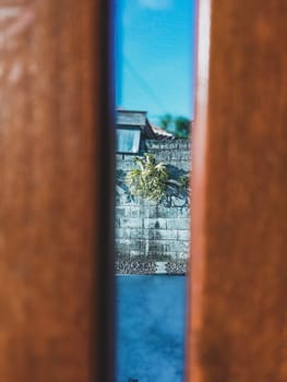 A unique view through a wooden fence reveals a garden with a stone wall backdrop. A single plant enhances the serene outdoor setting.