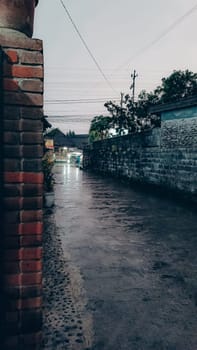 A tranquil urban street captured during a rainy evening, featuring wet pavement and dim lighting, conveying a peaceful and reflective atmosphere.