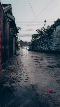 A tranquil urban street captured during a rainy evening, featuring wet pavement and dim lighting, conveying a peaceful and reflective atmosphere.