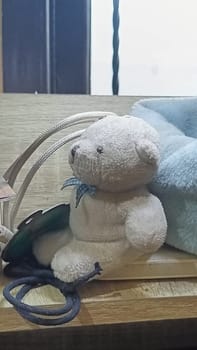 A teddy bear is sitting on a wooden surface next to a blue blanket. The scene is cozy and inviting, with the teddy bear looking up at the camera