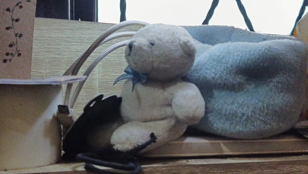 A teddy bear is sitting on a wooden surface next to a blue blanket. The scene is cozy and inviting, with the teddy bear looking up at the camera