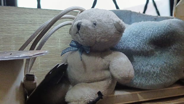 A teddy bear is sitting on a wooden surface next to a blue blanket. The scene is cozy and inviting, with the teddy bear looking up at the camera