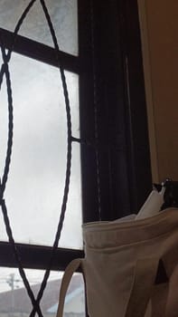 A window with a bag hanging from it. The bag is white and has a black strap