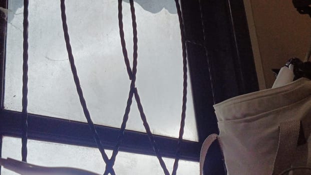 A window with a bag hanging from it. The bag is white and has a black strap