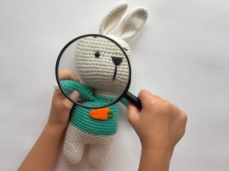 Child examining knitted bunny with magnifying glass for creative exploration.