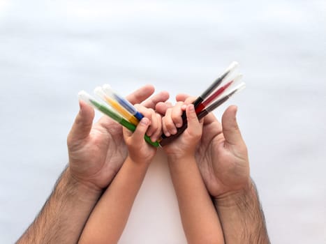Family bond. Adult and child hands holding colorful paint tubes together.